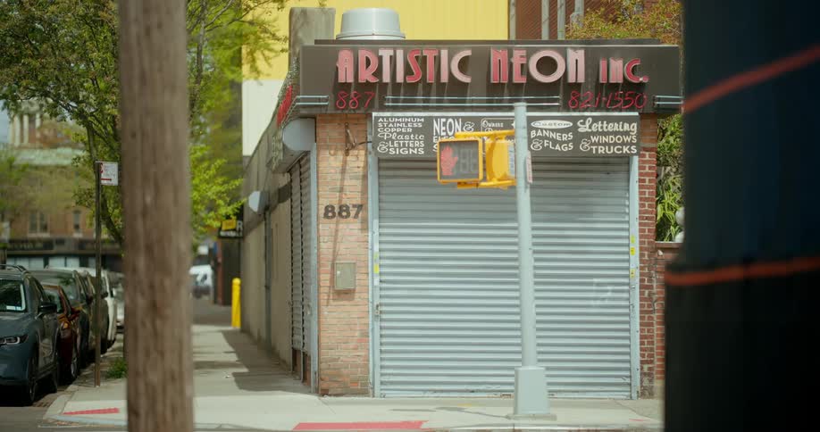 A car drives past a closed neon storefront in the city