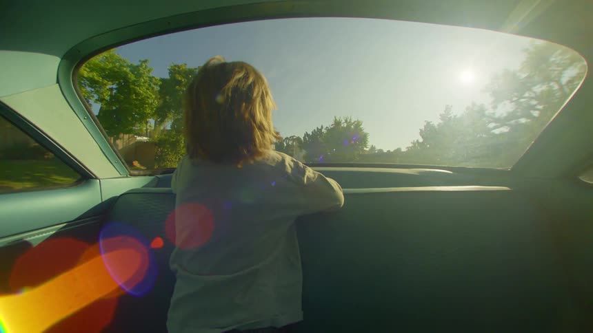 View from inside a moving car with a child looking out the rear window