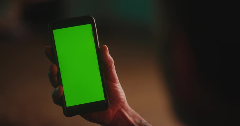 A human hand holding a cell phone with a completely green screen