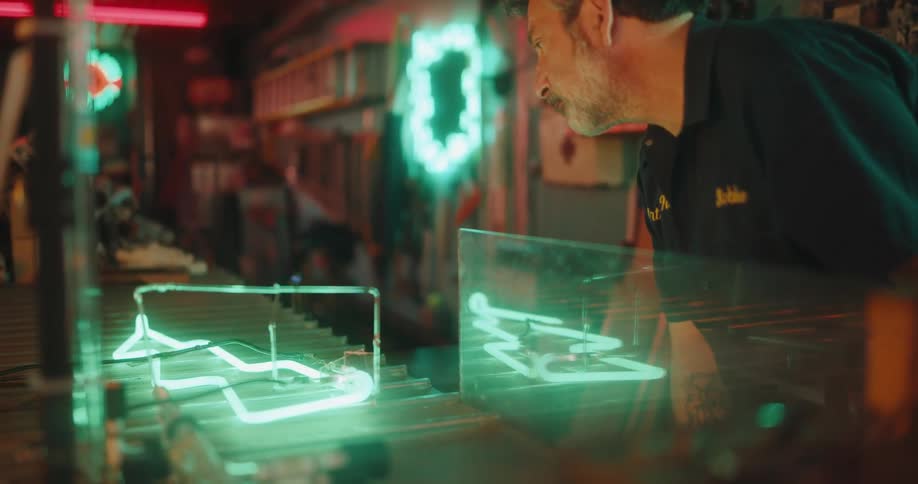 A worker at a neon tube manufacturing facility visually inspects a neon tube