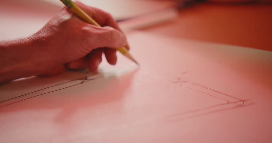 Hand holding a pencil and drawing geometric lines on a sheet of paper