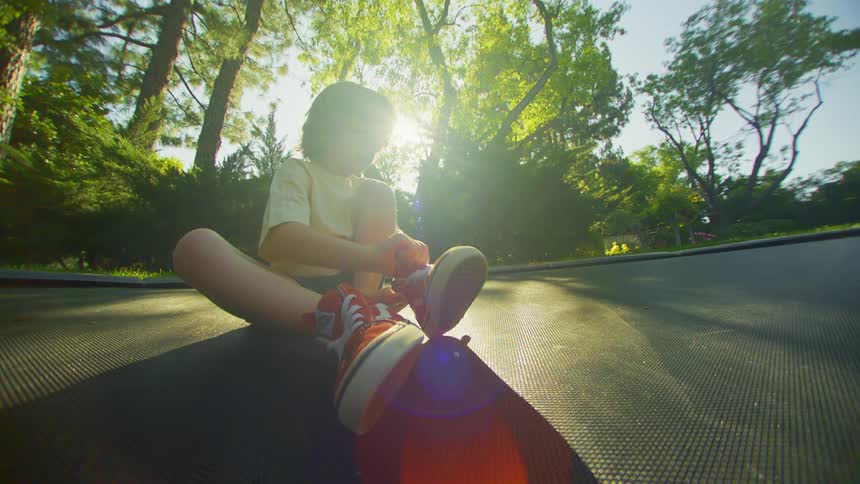 A young boy sitting on the floor of a park putting on his shoe