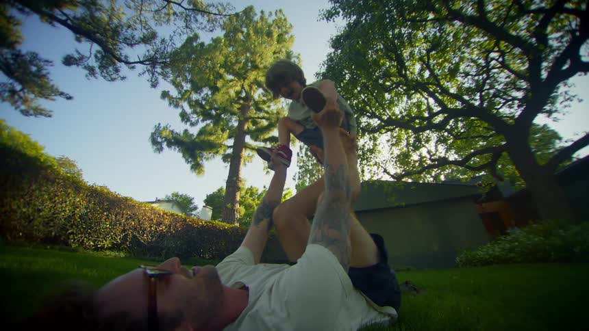 Man lying on the grass lifting a child into the air with his hands and feet