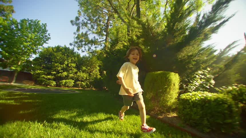 A young boy runs across a yard while laughing and smiling