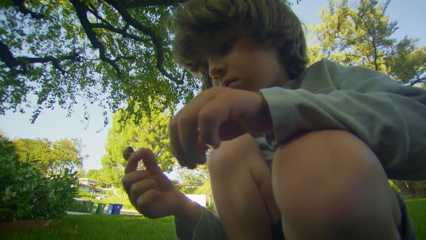 Little boy squatting in the grass picking a mushroom