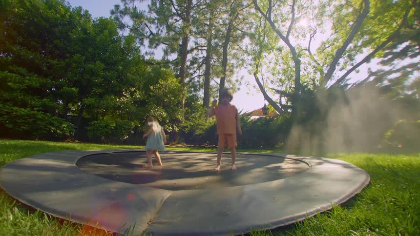 A boy and a girl jump on a ground trampoline in a yard