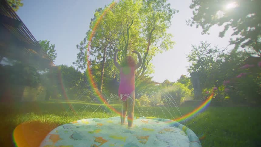 Little girl in a pool with water jets in the middle of a garden during the day