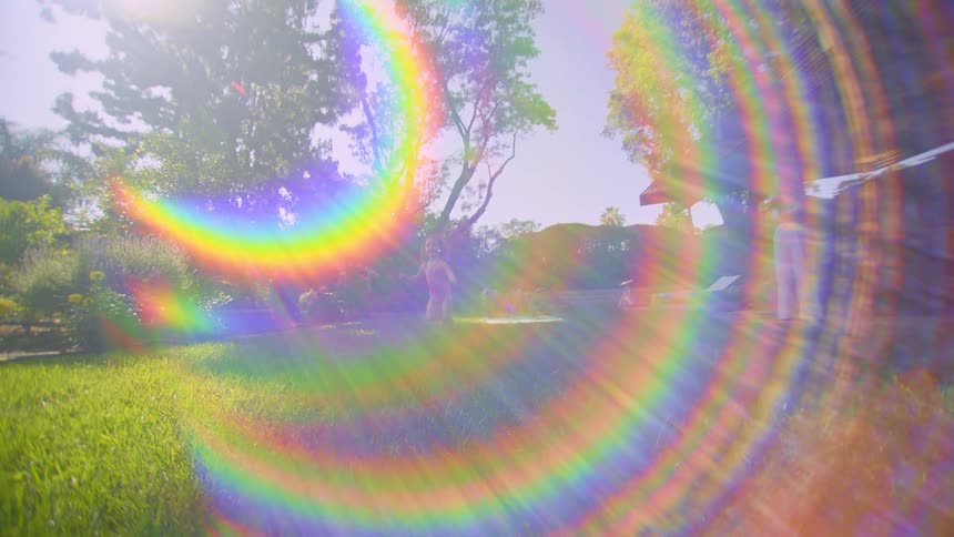 A little girl running in a yard with green grass and there is a flare of colored light in front