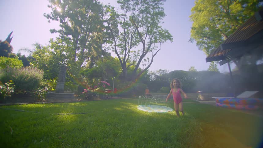 A little blonde girl in a swimsuit is running in a backyard that has a small pool and she is happy