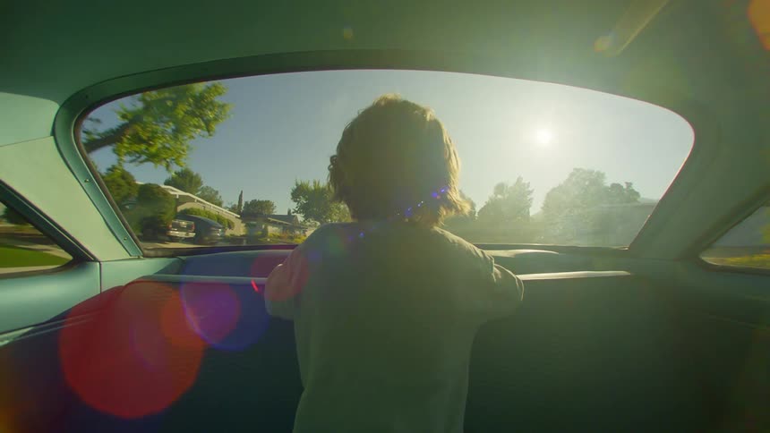 A little boy is sitting on the back of a car seat looking at the back window