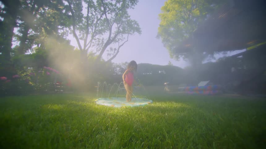 A little girl standing in a small pool in a yard with lots of grass