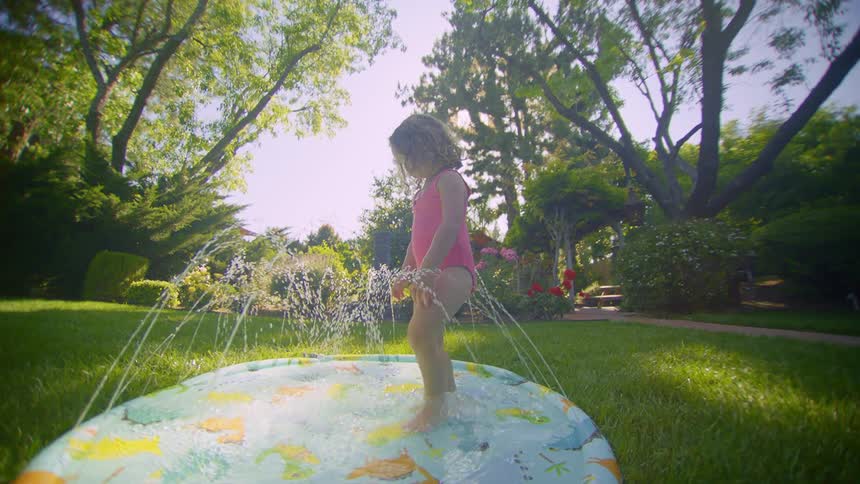 A child walks through the sprinkler in the yard
