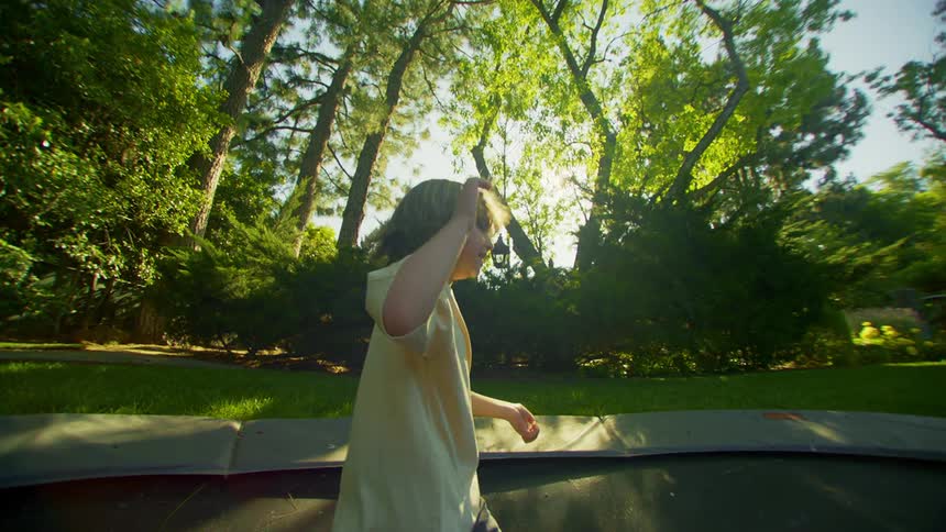 Little boy jumping on trampoline in the backyard with trees around