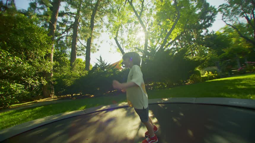 A young boy has fun jumping up and down on a ground trampoline in a yard
