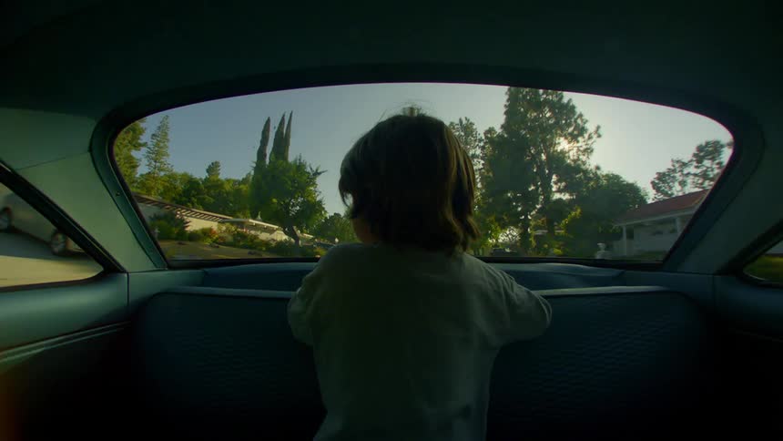 A child looks through the back window of the car as he rides