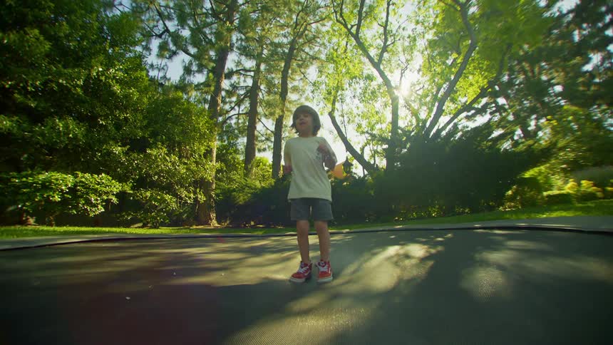 Kid smiles while jumping on a trampoline in the backyard on a sunny summer day