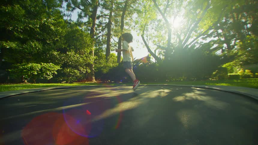 Little boy jumping on trampoline in a yard surrounded by trees