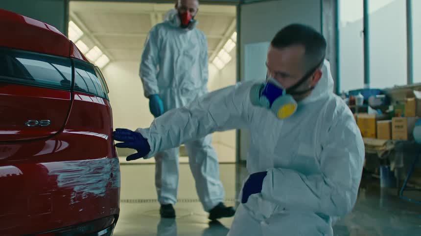 Men with protective mask and specific clothing checking the shaved rear end of a red car