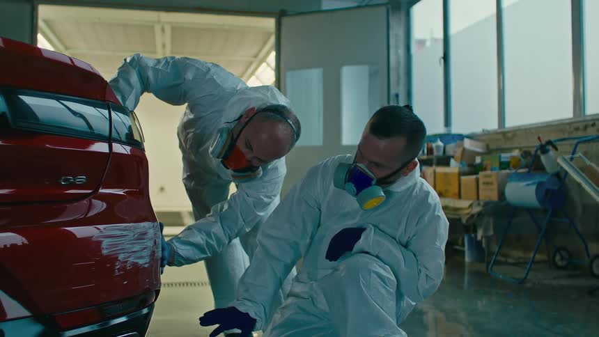 Two men with masks and specific clothing checking the rear bodywork of a shaved red car