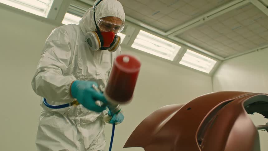 Man in protective clothing painting a part of a vehicle red