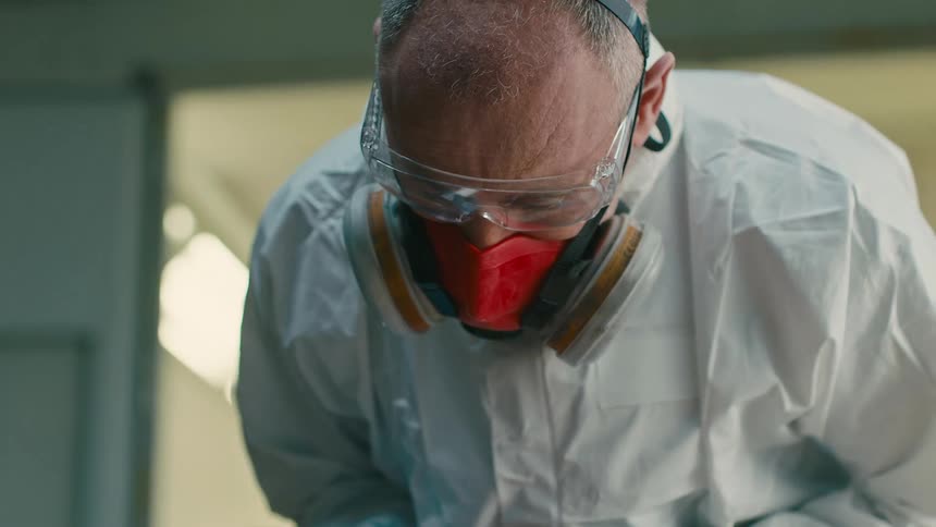Man with protective glove preparing red paint in a bottle and checking the reed with a metal plate