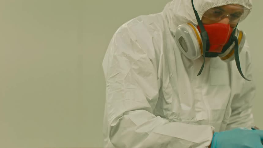 A man in a white protective suit with gloves sprays paint with a nozzle attached to a hose