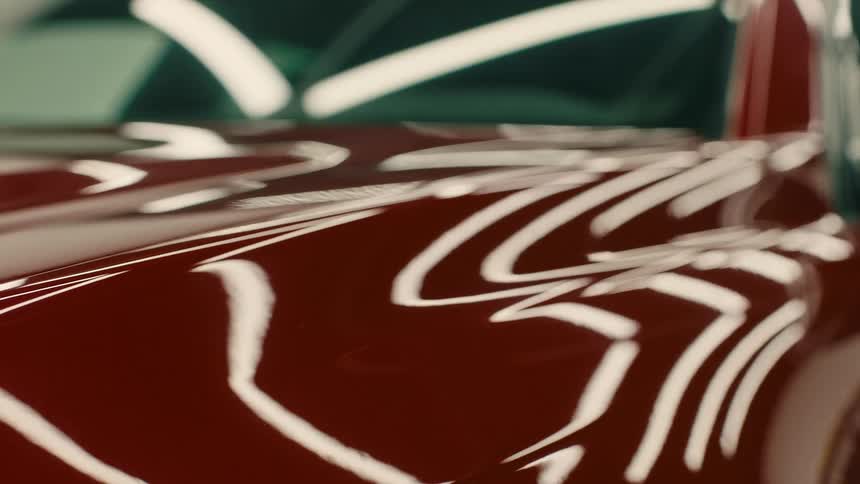 Closeup of a cars shiny red hood with reflections of white lights