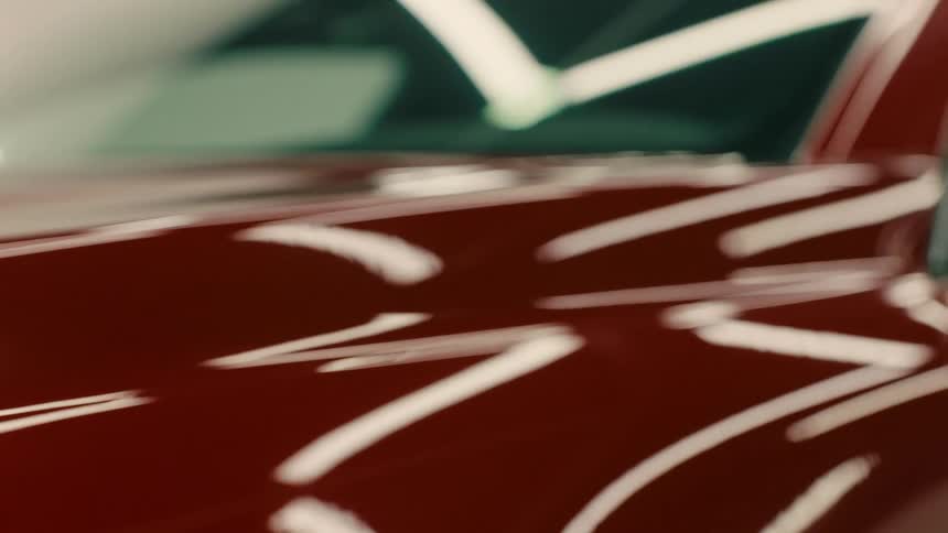 Closeup of the front of a red vehicle in an interior environment with reflected lights