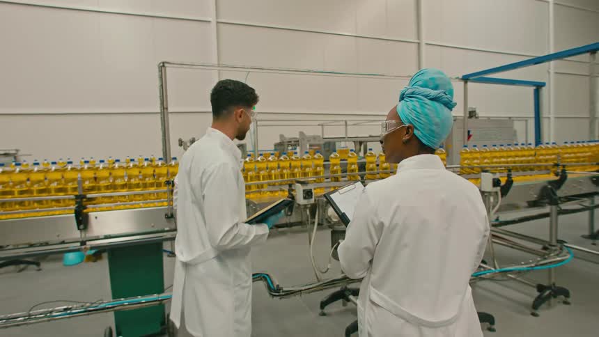 A couple of workers talk to each other in front of a cooking oil production line
