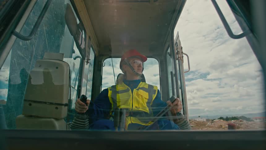 An woman wearing high visibility jacket and hard hat operating heavy machinery