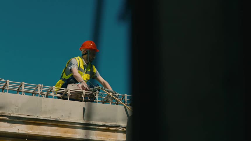 A construction worker in highvisibility gear working on a concrete structure with steel reinforcement