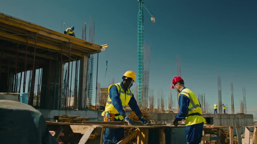 Construction workers in safety gear at a site with steel reinforcements and a crane