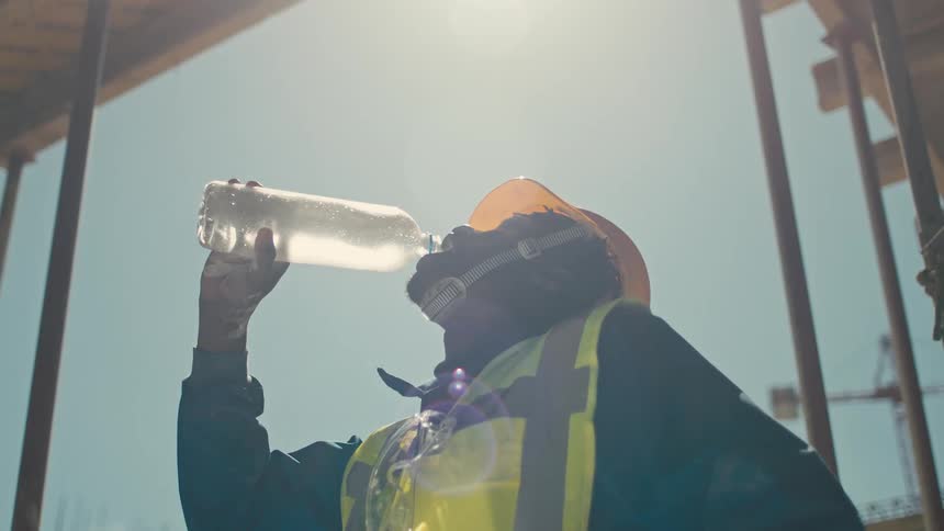 Worker on a construction site takes a break to drink water from a bottle