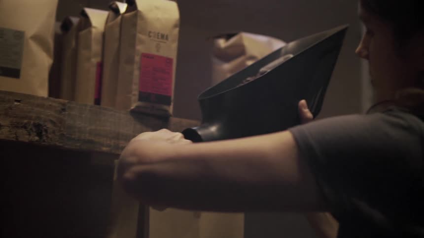 A woman walks over to a shelf and fills a bag with coffee beans