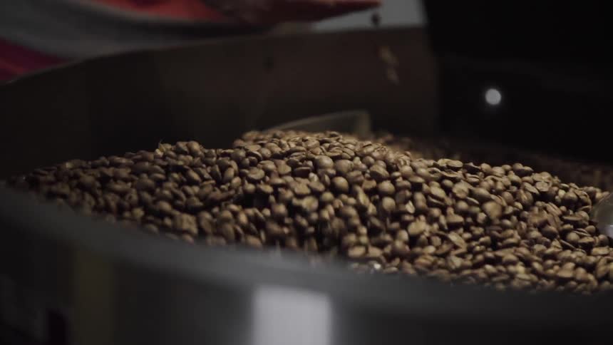 A man grabbing a few coffee beans as they are stirred in a machine