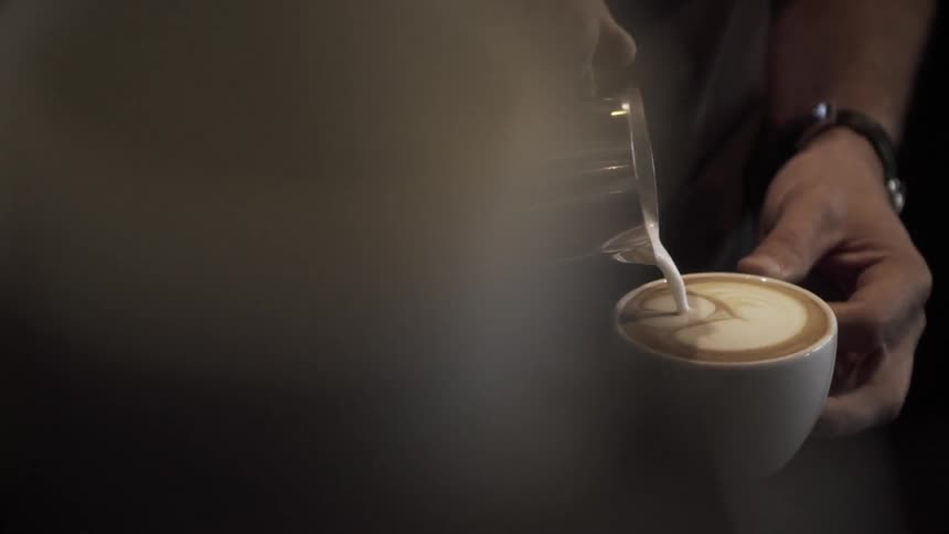 A person creates a heart shape in the foam in a cup of coffee