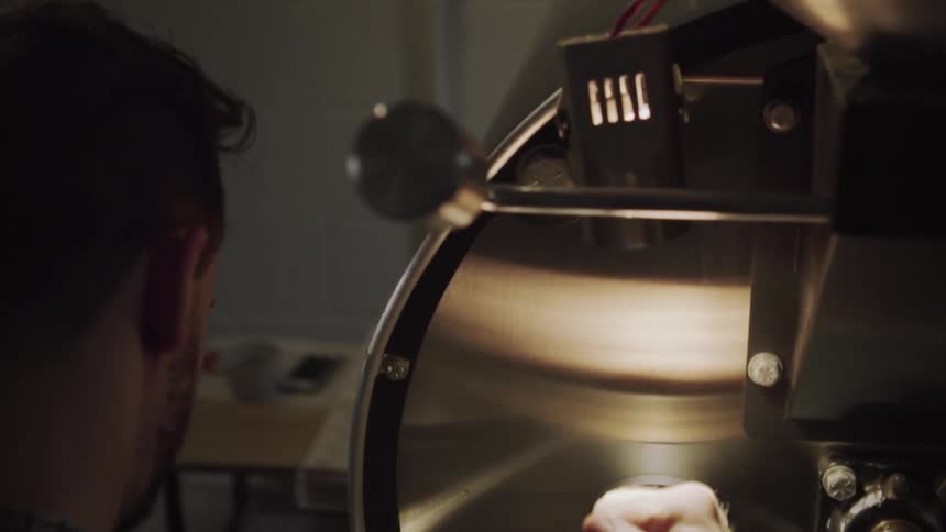 A man is operating a coffee roaster in a shop