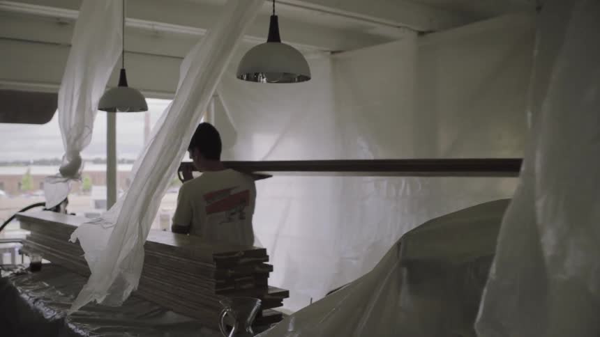 Two construction workers carry a board through a home