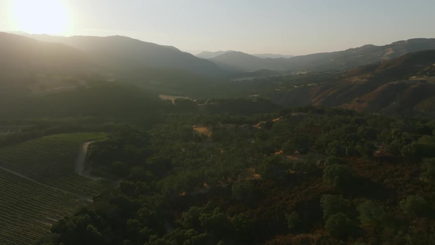 Aerial scenery of greenish mountains and hills with the sun on the horizon