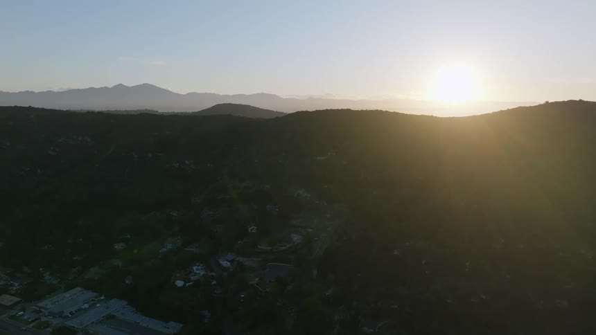 Town remains in shadow of low mountain as sun rises past top of mountain