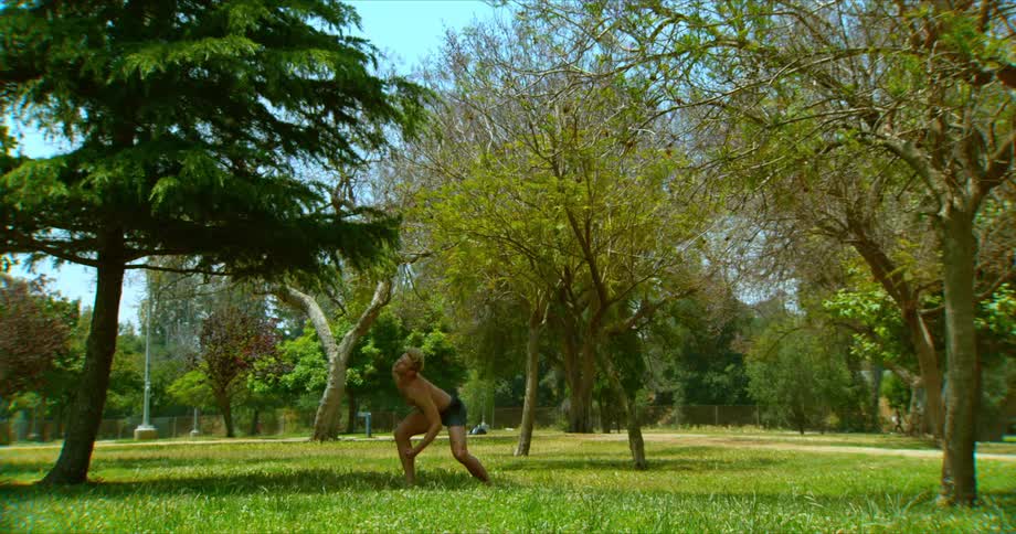 Man moves slowly into a new pose in tai chi under a few trees
