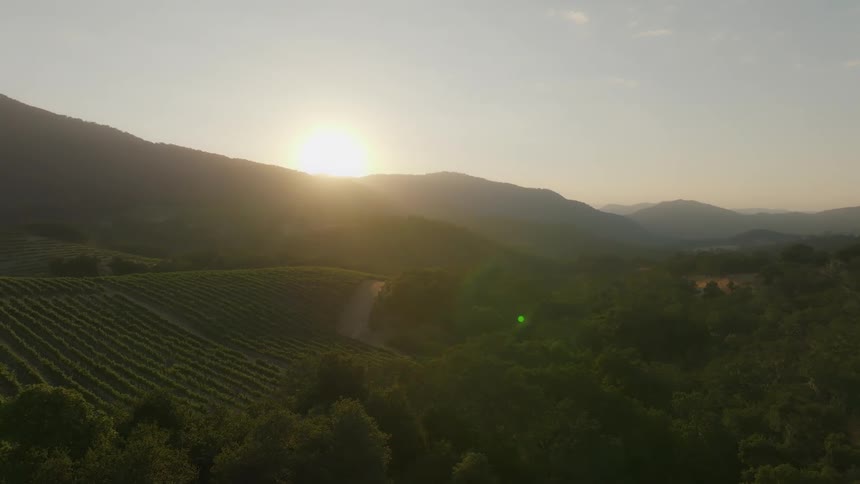 The sun emerges from behind the mountains behind a farm