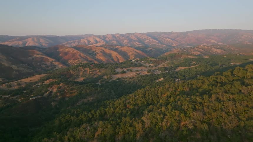A rural area with homes surrounded by a forest and mountain ranges