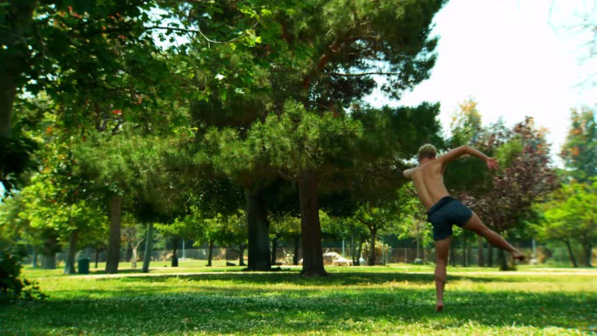 Male dancer spins while kicking one foot up on a cloudy day in the park