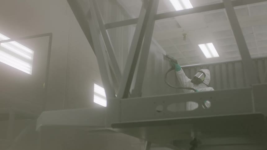Person wearing a mask and protective clothing performing painting in an indoor metallic environment