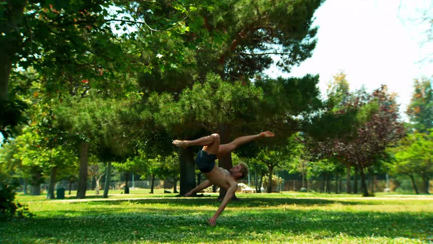A young man stretches in a park and then performs a body flip