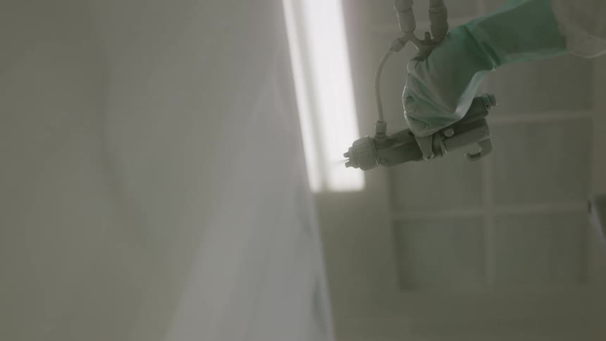 A worker uses a paint gun to paint a wall