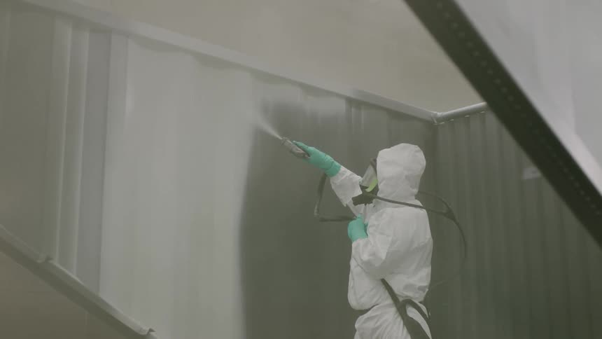 Person in white protective suit performing spray painting indoors
