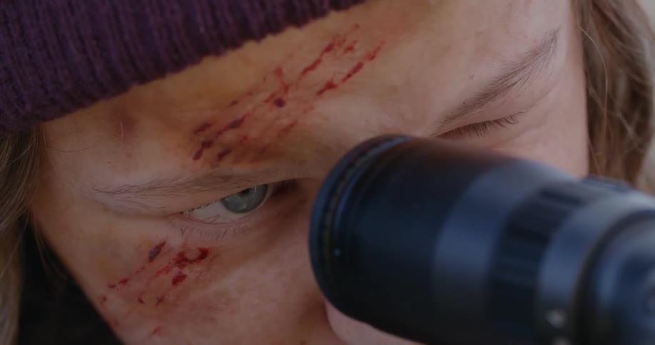 Closeup of a persons face with blood marks and concentrated looking into the scope of a sniper gun