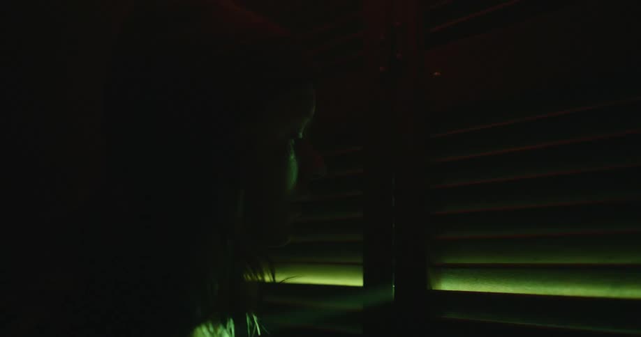 Silhouette of a woman looking at a window passing beams of lights in a dark room